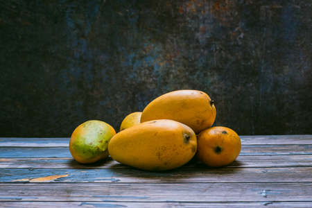 Group of ripe mangoes in dark environment on wooden table. Sideview.