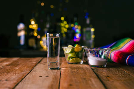 Shot of tequila served in a tequila glass on a wooden table. Blurred background. Rustic bar atmosphere.の写真素材