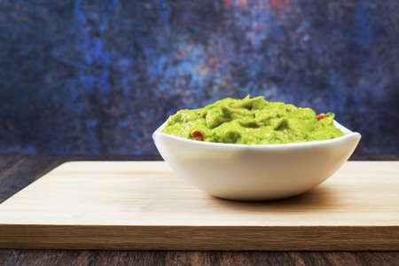Guacamole served on white plate on wooden table. Insulated container with guacamole.の写真素材