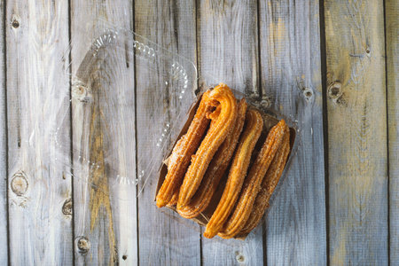 Churros in a plastic container on a wooden table. Homemade churros.の写真素材