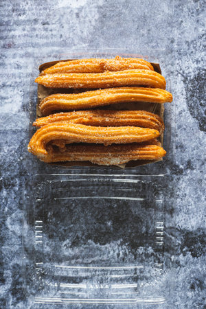 Churros in a plastic container on a cement table. Churros ready to eat.の写真素材