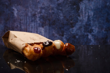 Stuffed churros on black table with reflection. Churros in paper bag. Blue background.