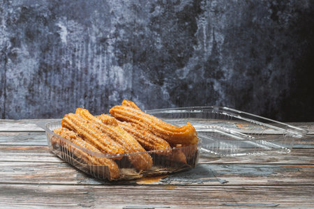 Churros in a plastic container on a wooden table. Homemade churros.