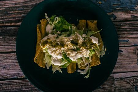 Flute tacos with cheese, cream and lettuce on a wooden table. Mexican snacks.