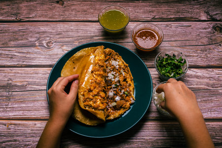 Hands of a person preparing a gringa pastor a la diabla accompanied by sauces and other condiments on a wooden table. Gringo, typical Mexican dish.の写真素材
