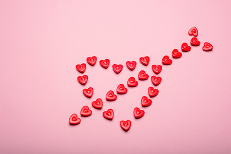 Heart-shaped frame made with small hearts crossed with an arrow on a pink background.