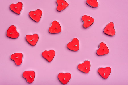 Group of heart-shaped scented candles extinguished on a pink background.