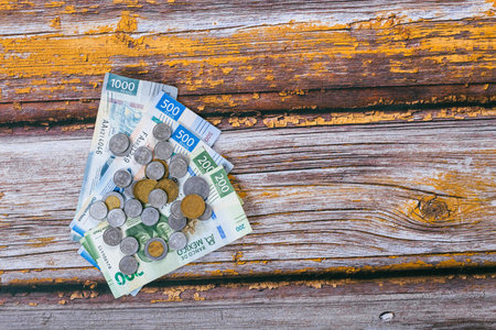 Stack of Mexican coins and bills on wooden table.