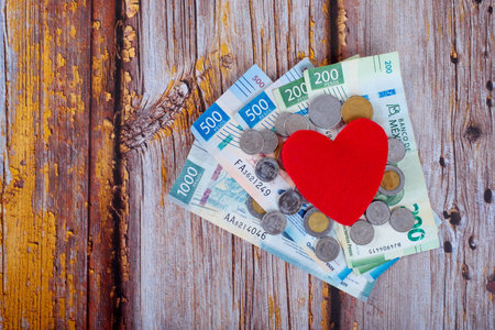 Heart next to a pile of Mexican pesos on a wooden table. Cost of health concept.の写真素材