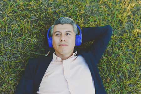 Portrait of a man lying on the grass listening to music with headphones.の写真素材