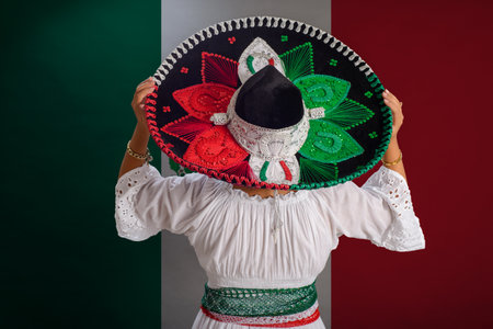 Woman shows Mexican hat with the colors of the Mexican flag. Mexican flag in background.の写真素材