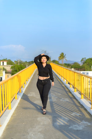 Portrait of young woman wearing a hat with positive attitude on a pedestrian bridge. Sunset with blue sky.の写真素材
