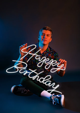 Studio portrait with neon lights of man with luminous happy birthday sign. Man celebrating his...