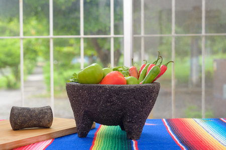Molcajete with vegetables on a colorful serape. Ingredients for a hot sauce.の写真素材