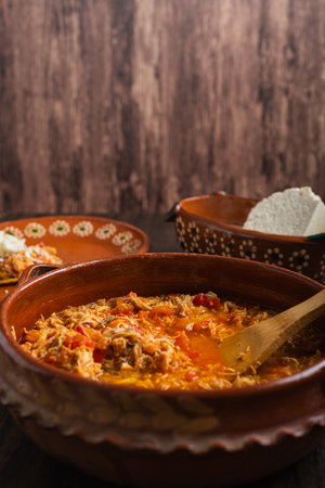 Authentic mexican chicken tinga, typical mexican food prepared in a clay pot on a wooden table.の写真素材