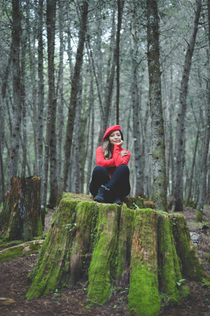 Woman in a calm and thoughtful attitude on a mossy stump in the middle of the forest.の写真素材