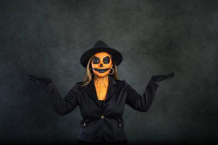 Woman made up as a pumpkin to celebrate Halloween pretending to hold something in her hands. Dark background with copy space.の写真素材