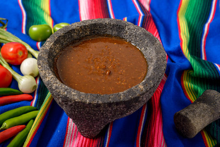 Molcajete with sauce and vegetables around it on a colorful serape. Ingredients for a hot sauce.の写真素材