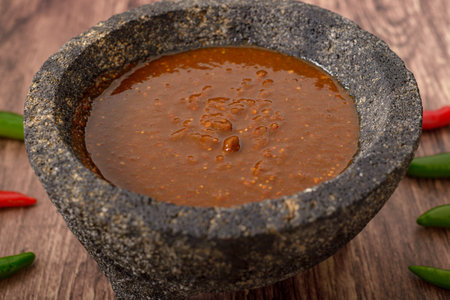 Molcajete with hot sauce on wooden table with chili peppers around.の写真素材