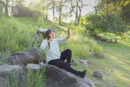 Woman taking a selfie seated on a rock in the middle of nature.の写真素材