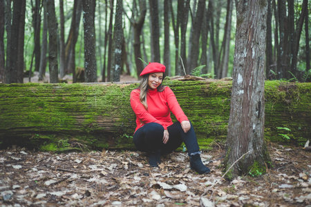 Smiling woman reclining on a mossy tree trunk in the middle of the forest looking at the camera.の写真素材