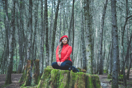 Woman in a calm and thoughtful attitude on a mossy stump in the middle of the forest.の写真素材