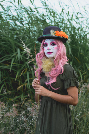 Young woman made up as a sad clown in a lonely field. Concept of loneliness and sadness. Halloween...