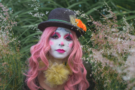 Young woman made up as a sad clown in a lonely field. Concept of loneliness and sadness. Halloween makeup.の写真素材