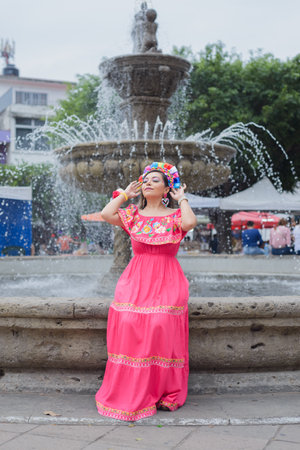 Street portrait of Mexican woman wearing traditional dress with multicolored embroidery. Hispanic woman celebrating the day of the beginning of the Mexican Revolution.の写真素材