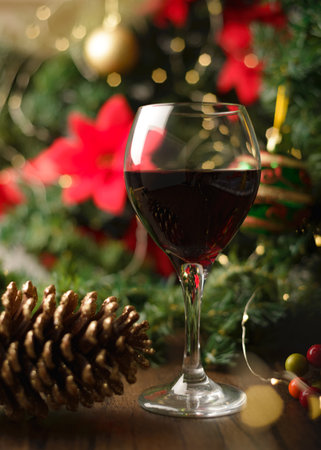 Glass of red wine on wooden table with Christmas decorations. Christmas tree and lights in the background.の写真素材