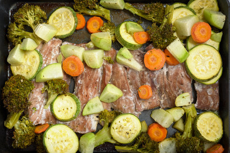 Tray with fish fillets and vegetables baked on a wooden table. Healthy food.の写真素材