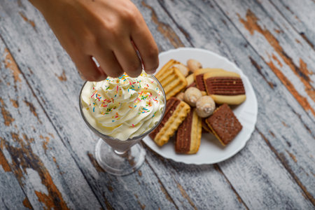 Person adding sprinkles to a chocolate milkshake. Milkshake with whipped cream on a wooden table.の写真素材