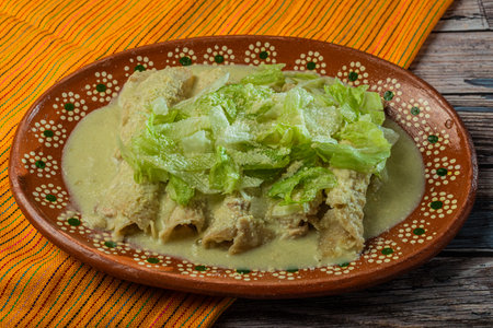 Green Enchiladas with lettuce served in a clay dish on a wooden table.