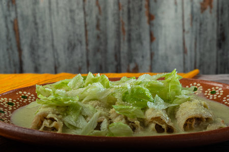 Green Enchiladas with lettuce served in a clay dish on a wooden table.