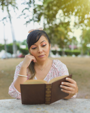 Woman sitting at a park table reading a book. World book day. Concept of reading.の写真素材