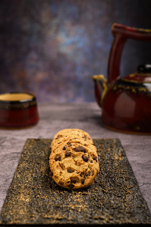 Vanilla chocolate chip cookies with tea set in the background on cement table.