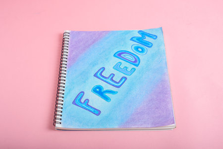 Notebook with the word freedom drawn with colored chalk. Painted notebook on pink background.の写真素材