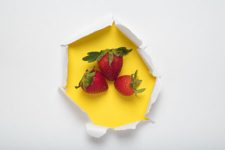 White paper with torn hole revealing strawberries on yellow background.の写真素材