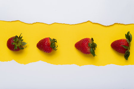 Strawberries on yellow background with turned white paper edges. Space for text. Summer background.の写真素材