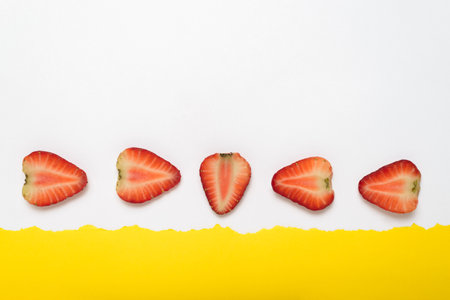 Sliced strawberries on yellow background with turned white paper border. Summer background.の写真素材