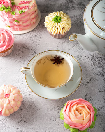 Mug with anise tea surrounded by colorful desserts. Several cupcakes decorated with buttercream.の写真素材