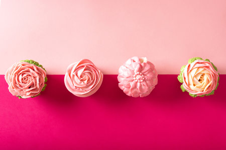 Colorful cupcakes on vibrant colored paper background. Decoration shaped like flowers with buttercream frosting.の写真素材