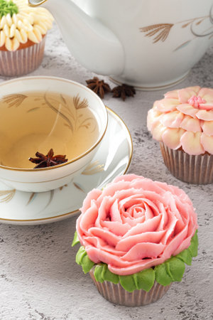 Colorful cupcakes with flower decorations made with buttercream, cup and teapot on the side.の写真素材