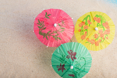 Colorful cocktail umbrellas on sea sand. Vacation concept. Summer background.