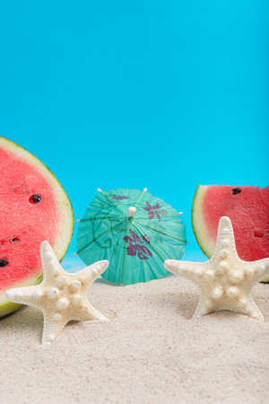 Watermelon slice with cocktail umbrella on sea sand with blue background. Summer background.の写真素材