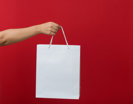 Female hand holding a shopping bag. Red background.の写真素材