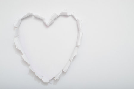 Heart-shaped hole turned in the center on white paper revealing a white background. Copy space.の写真素材