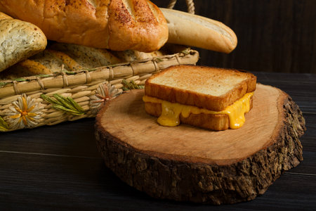 Grilled cheese sandwich on a rustic wooden plate with a basket of bread in the background. Copy...