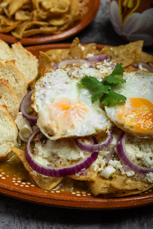 Chilaquiles, typical Mexican food, served in a clay dish with fried eggs and bread.の写真素材