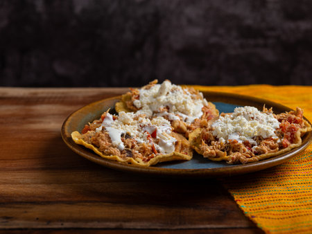 Tostadas with chicken tinga, cheese and cream on a plate on a wooden table. Typical Mexican food.